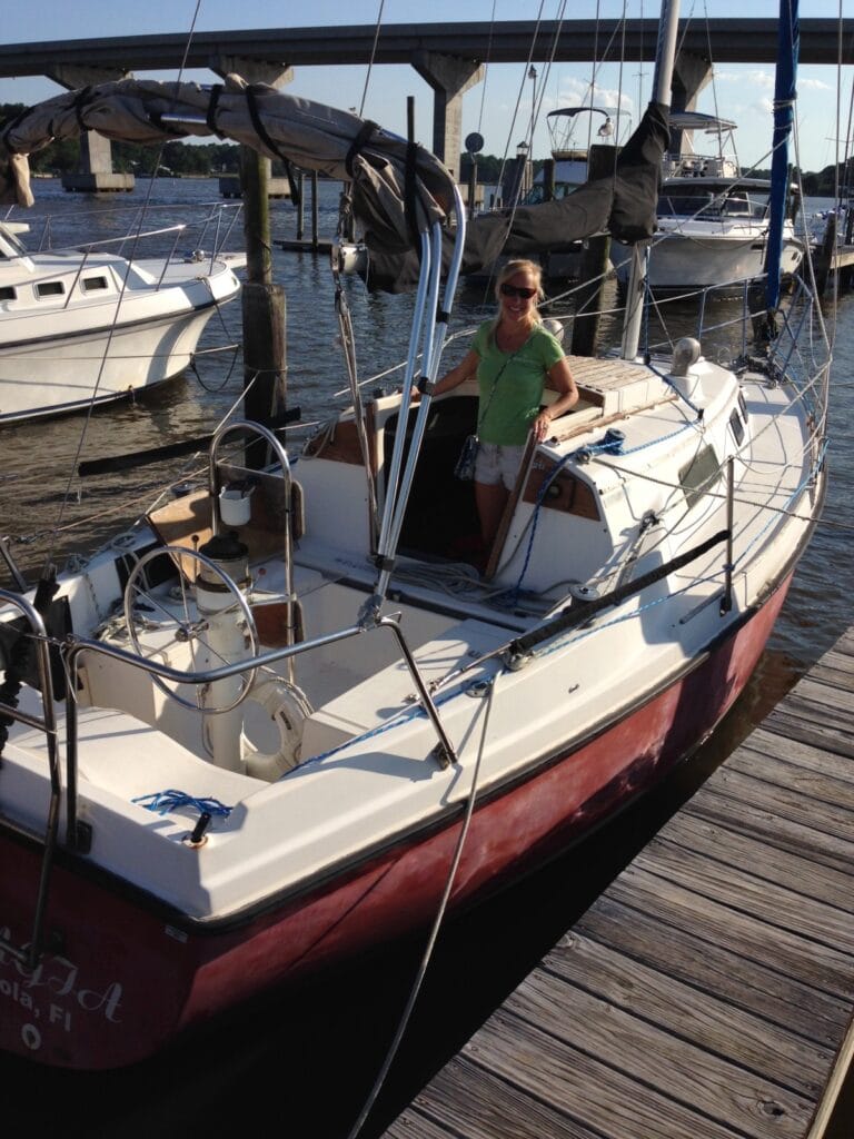 Photo of me, Jill, standing in the companionway of our 26 foot sailboat Pelagia. The sailboat is a Seafarer with old red paint that needs a really bad wax job!