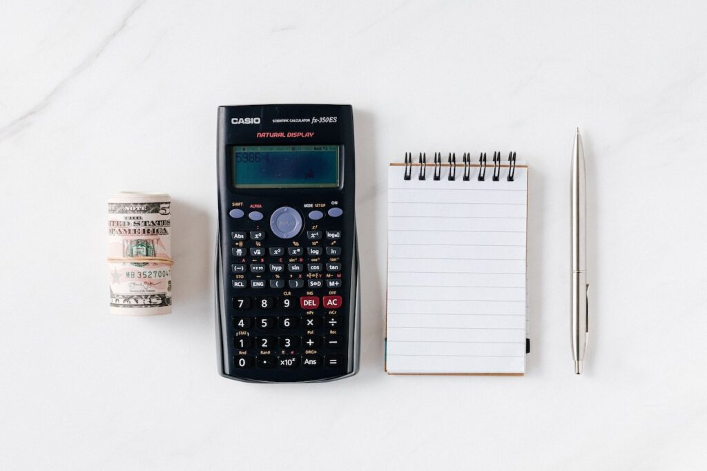 Photo of a wad of money, calculator, note pad and pen on a white background