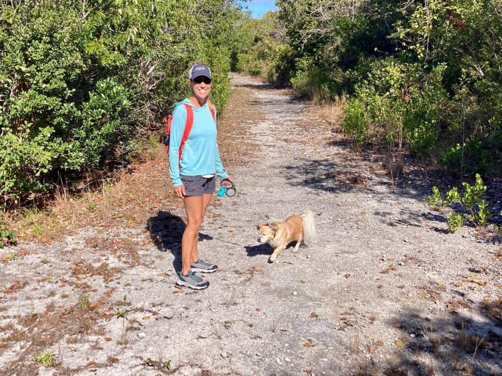 Mangaux and me walking down a path lined with trees and scrub shrub on Cistern Cay on a sunny day.
