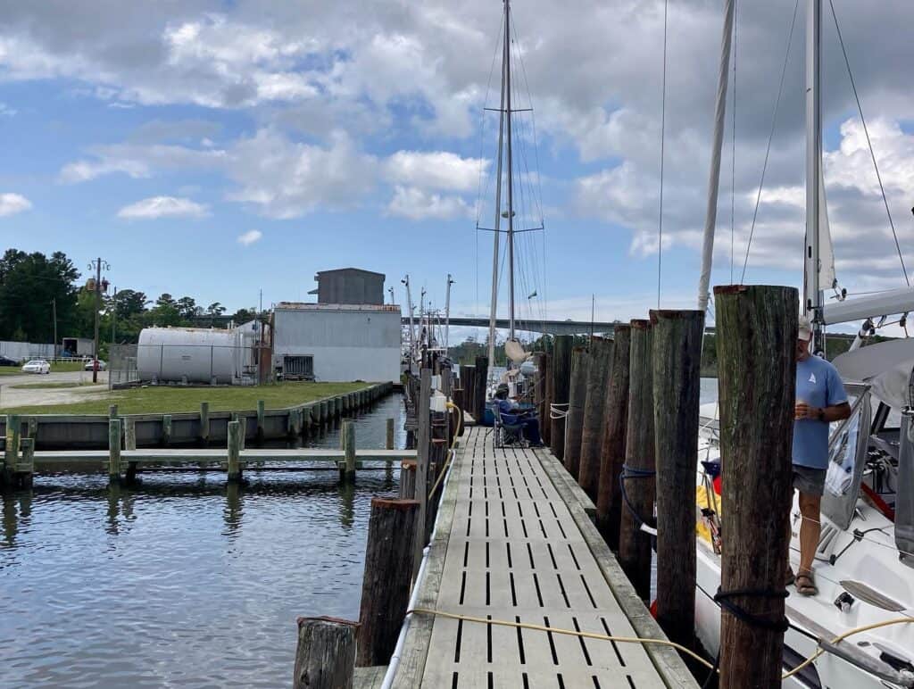 The fixed dock at RE Mayo with tall wooden pilings. The RE Mayo building is in the background. To the right is our buddy boat SV Alaina with Daryl standing on the port side deck of the boat.
