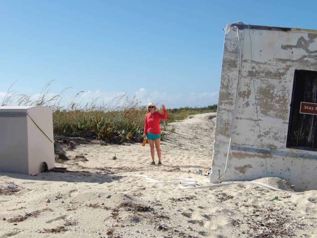 Casie is standing on a sandy trail on the Dry Tortugas waving at the camera. She is smiling, wearing a pink shirt and teal shorts.