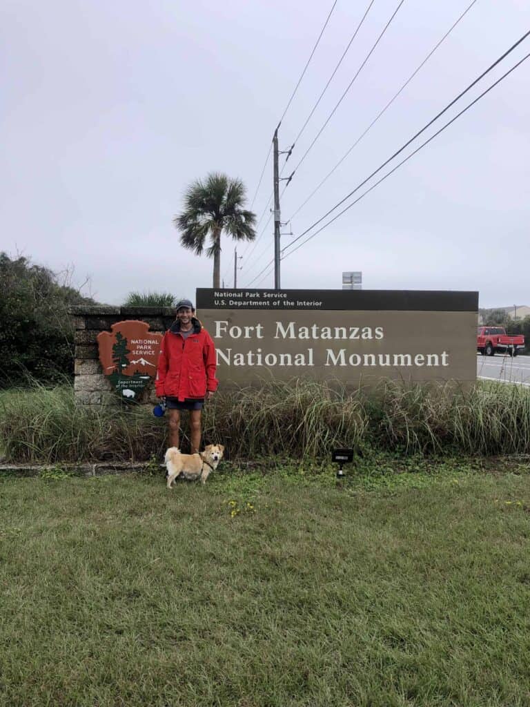 Scott in his red raincoat and Mangaux are standing in front of the Fort Matanzas National Monument Sign. We had great dog walking access at this anchorage.
