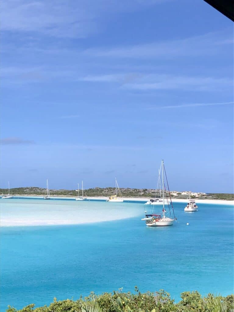 Several sailboats are moored at the Warderick Wells north mooring field, a narrow channel in clear blue waters on a sunny day.