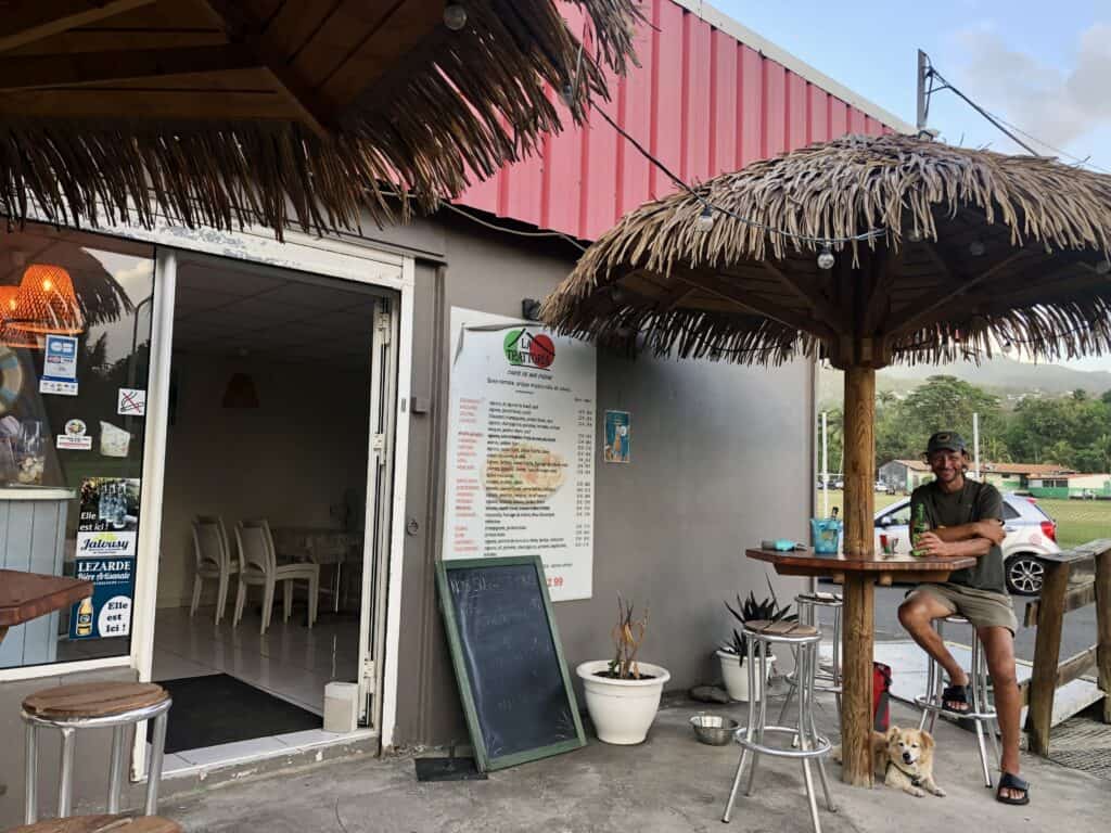 Amazing pizza place we found in Malendure, with Scott sitting under a straw umbrella table.