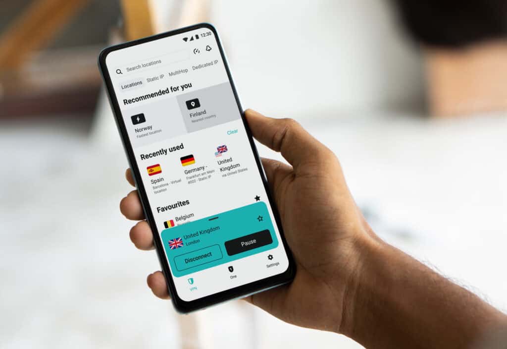 Person holding a smartphone with the Surfshark VPN mobile app open and connected to a United Kingdom server in London. The Surfshark Review example shows recommended VPN locations including Norway and Finland along with recently used servers.