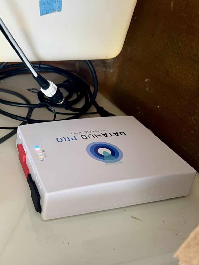 PredictWind DataHub Pro installed horizontally in the electronics compartment behind the helm with its indicator lights on and cables connected. The horizontal mounting position follows PredictWind's recommendation for DataHub Pro installation.
