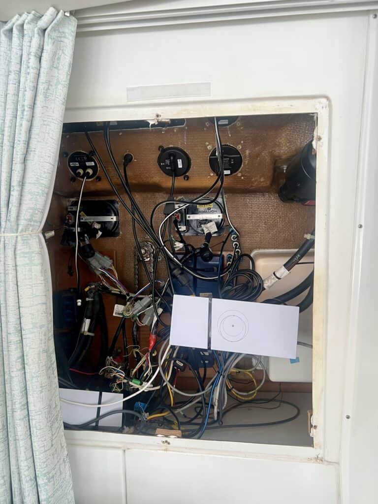 Open electronics compartment behind the helm station in the salon showing wiring and existing marine electronics where the DataHub Pro will be installed and connected to the Raymarine system. The Starlink router is also mounted in this compartment near the planned DataHub Pro installation location.