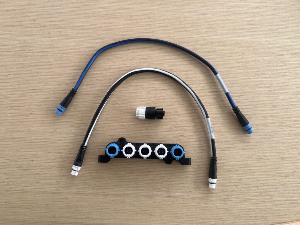 Raymarine cables and connector block laid out on a wooden table for the DataHub Pro installation. These parts were needed to connect our boat's existing Raymarine electronics to the PredictWind DataHub Pro.